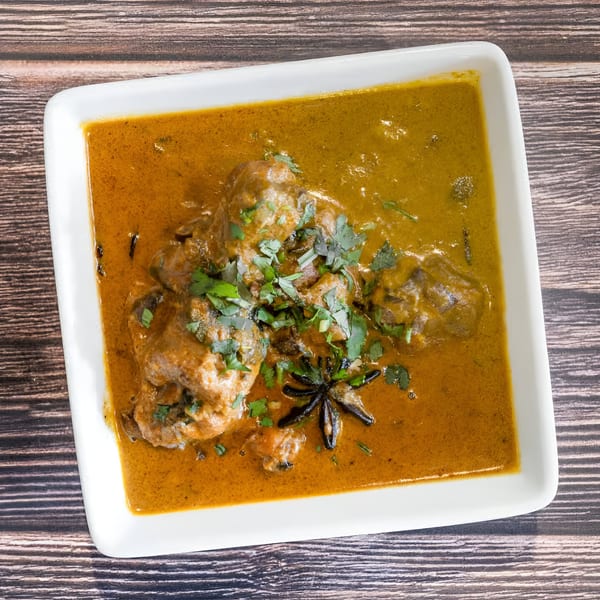 Avasa's Indian curry with meat, garnished with cilantro and star anise, in a white rectangular dish.