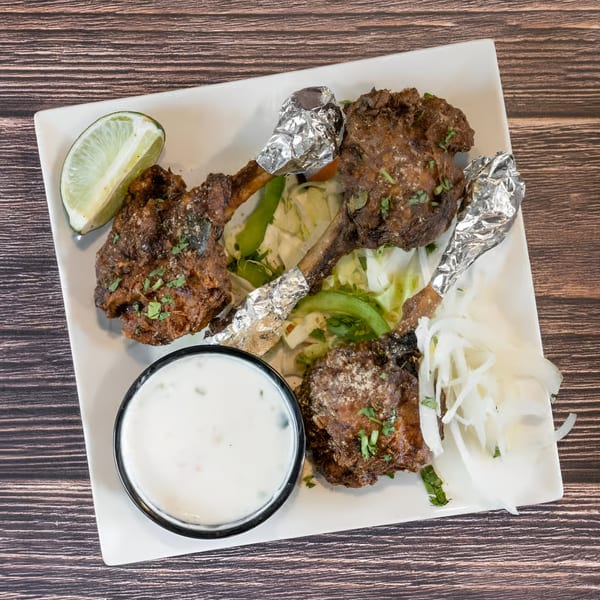 Avasa's Indian chicken lollipops with foil-wrapped bones, lime, salad, and a white dipping sauce.