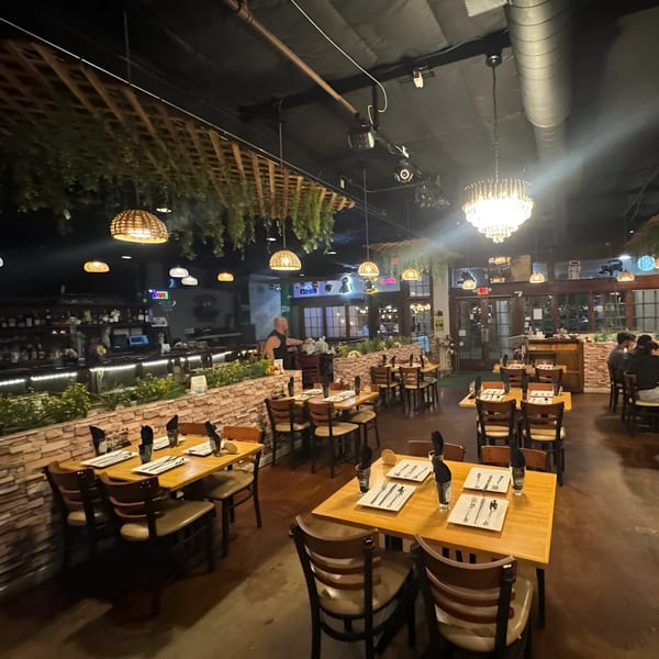 Avasa's dimly lit Indian restaurant interior features wooden tables, chairs, and a bar, with hanging plants and chandeliers.
