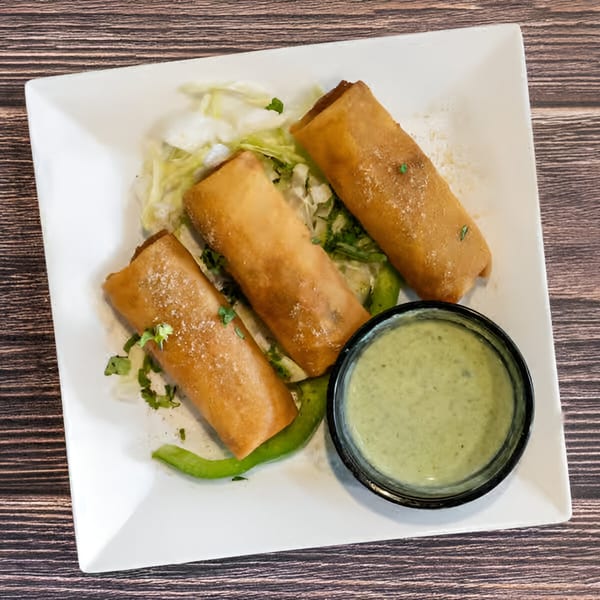 Three golden-brown spring rolls on a bed of lettuce with a side of green dipping sauce.