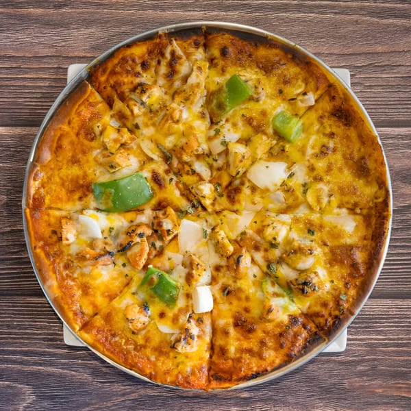 Avasa's Indian-style pizza, topped with chicken, onions, green peppers, and melted cheese, on a wooden table.