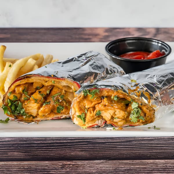 Two Indian chicken wraps, partially unwrapped from foil, served with fries and ketchup on a white plate.