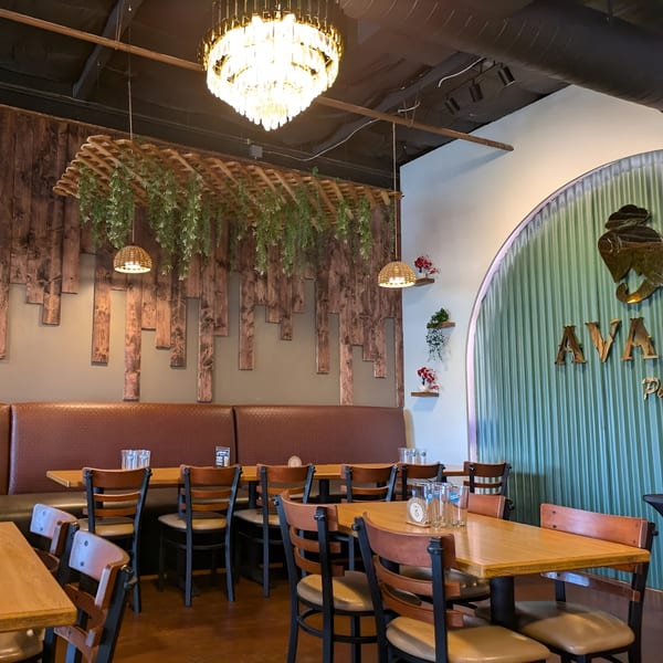 Avasa restaurant interior with wooden tables, brown chairs, and a decorative wooden wall with greenery.