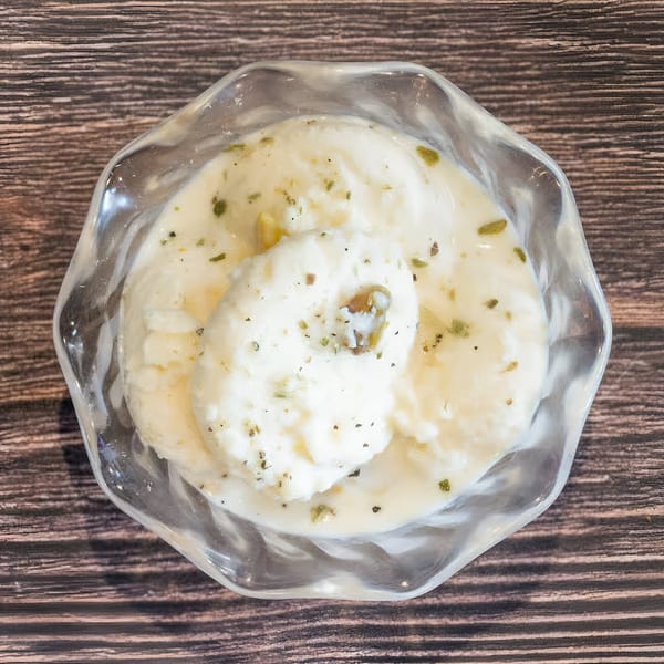 Top-down view of creamy Indian kulfi ice cream with green pistachio pieces in a clear glass bowl.