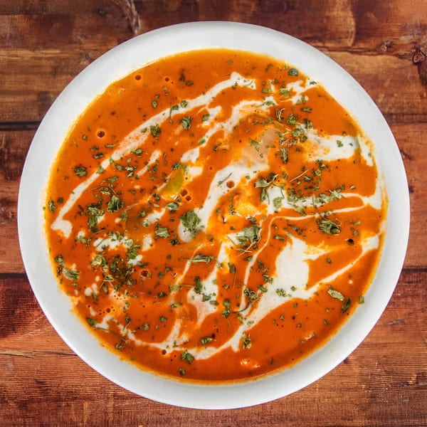 Overhead view of Avasa's Indian butter chicken, garnished with cream swirls and herbs.